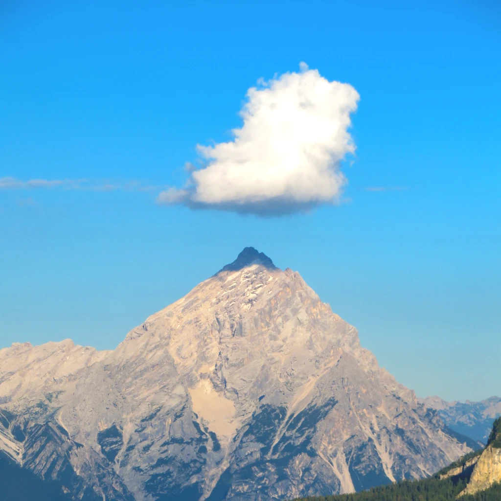 A small white cloud floating like a hat above a mountain peak