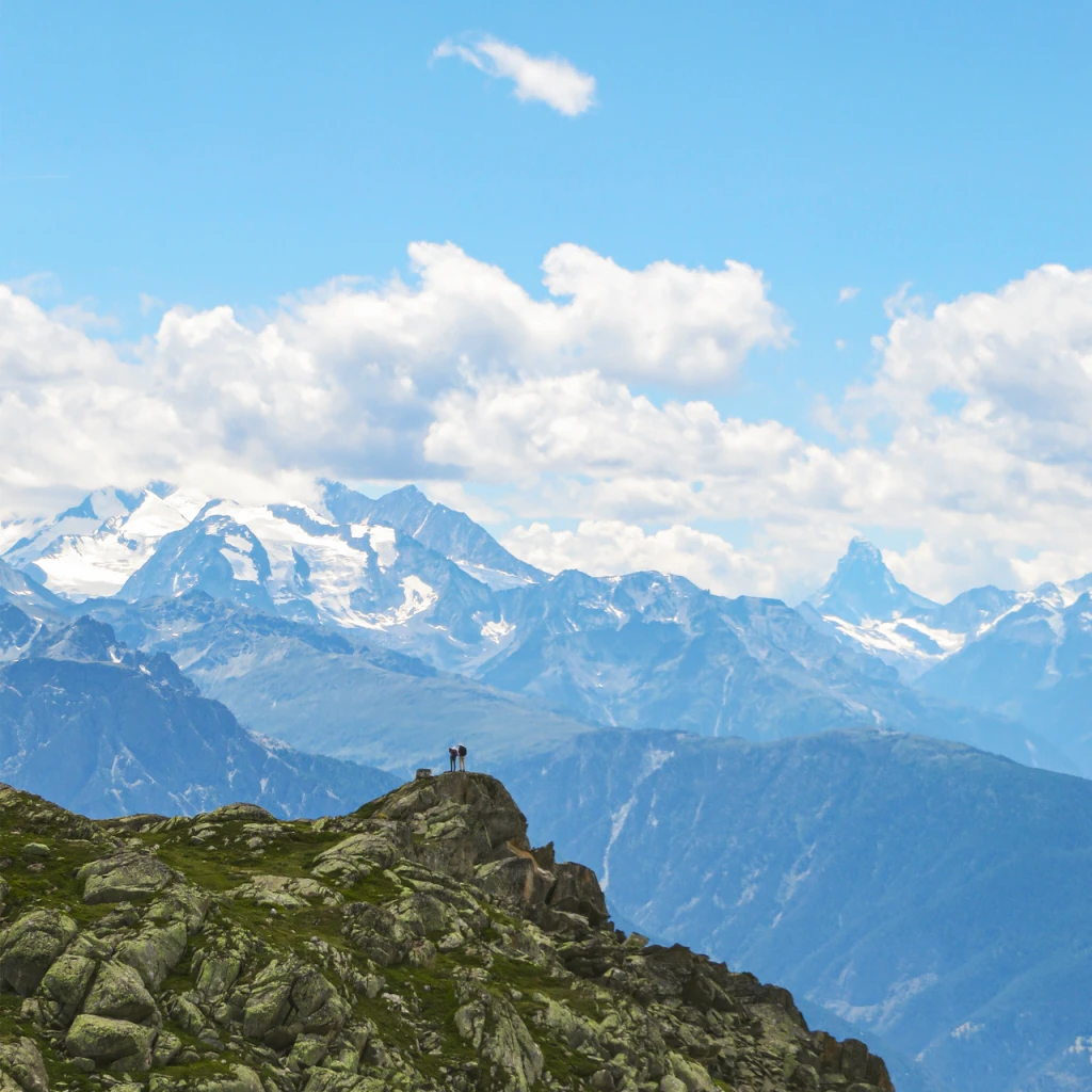 Two hikers perched on a rocky outcrop above the mountains