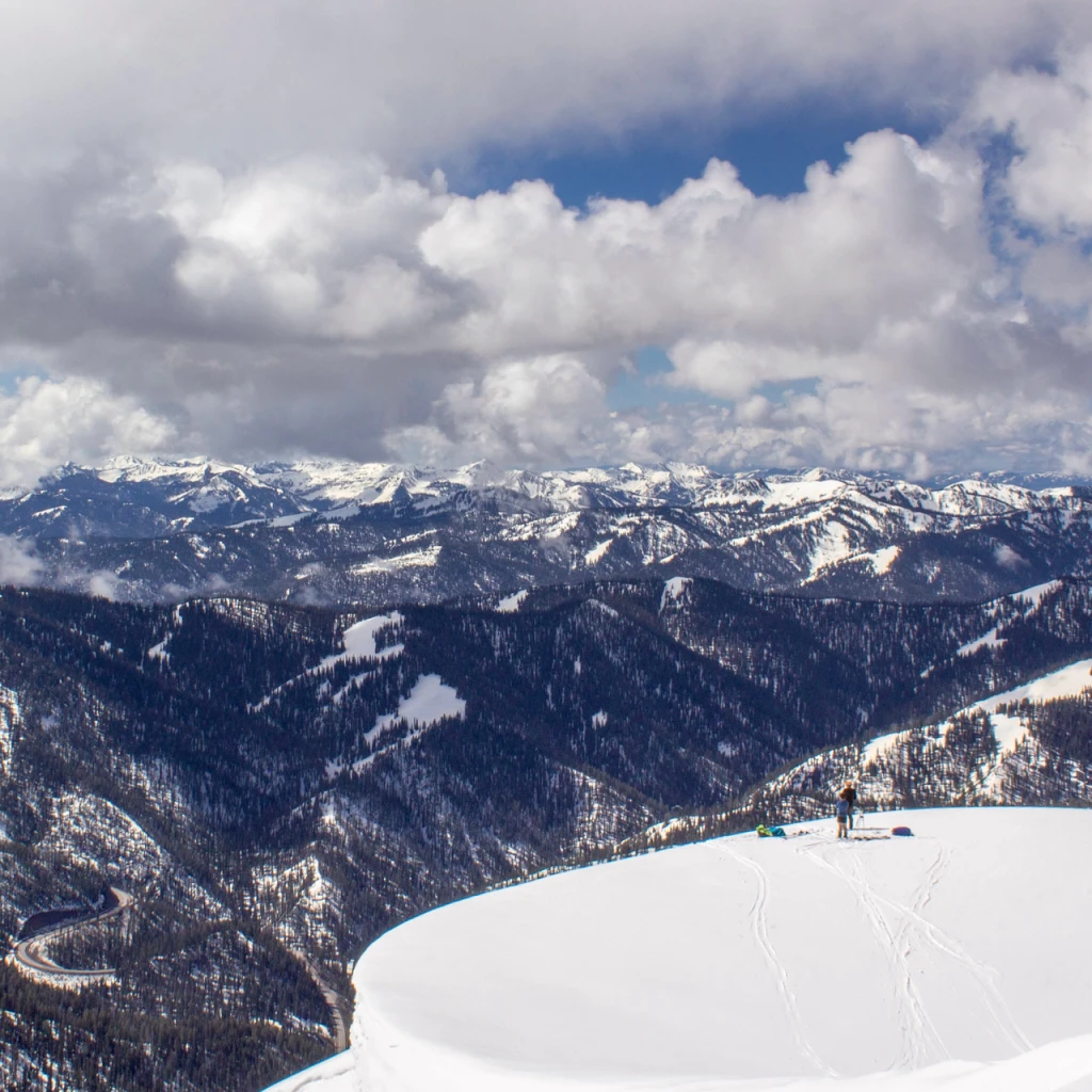 A skier on a snowy ridge overlooking the Tetons
