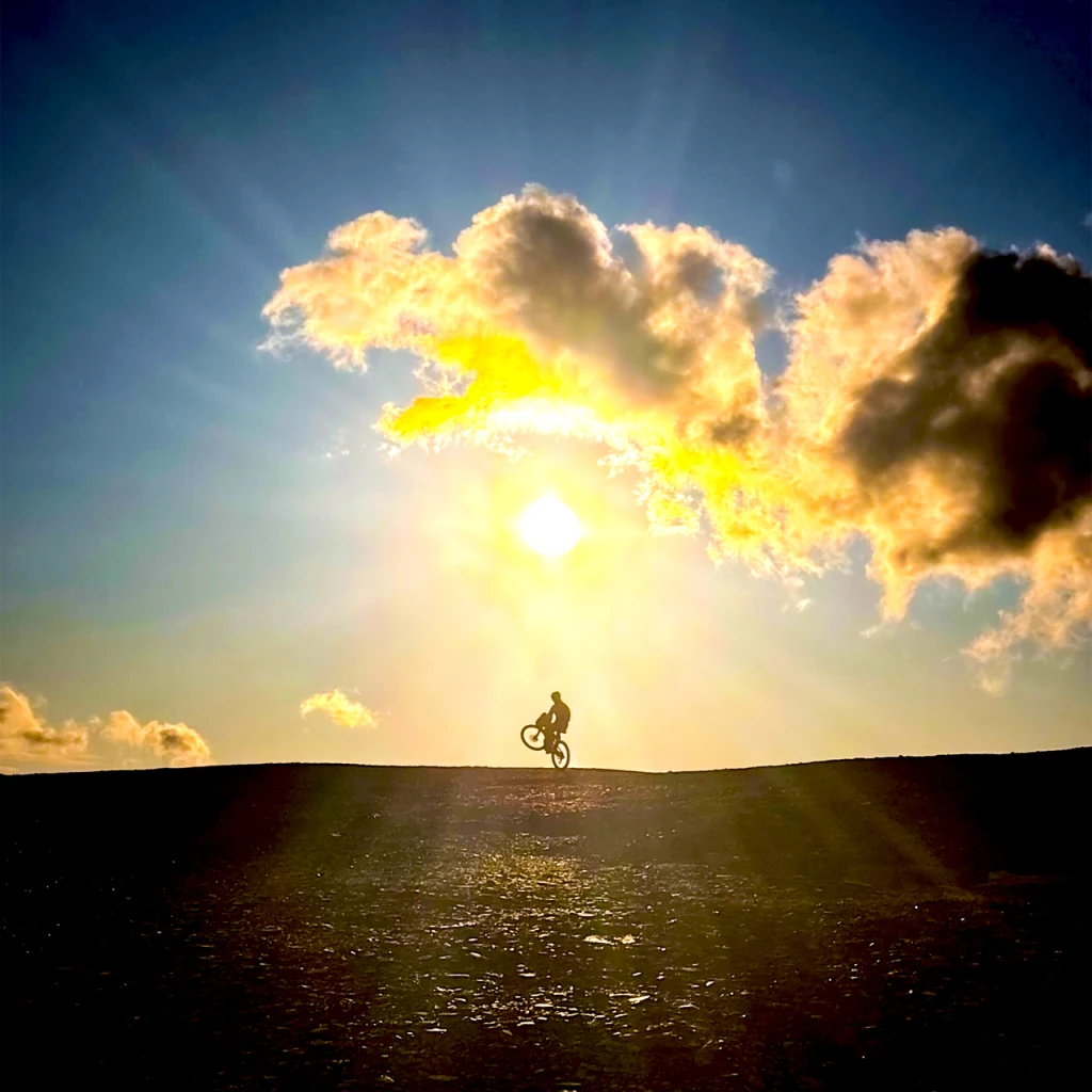 A cyclist doing a wheelie against the setting sun